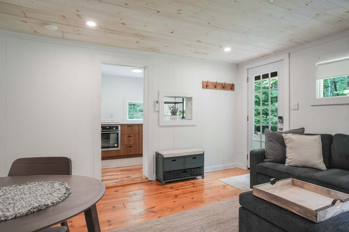 The living room from the dining table: a charcoal sectional, wide-plank floors, and the kitchen through the doorway