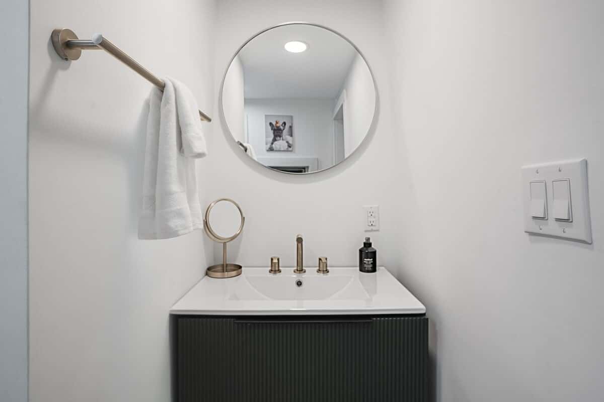 The bathroom vanity: a black fluted cabinet, brass fixtures, and a round mirror