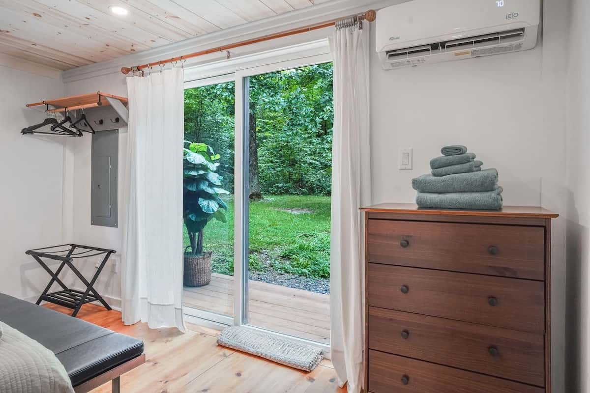 Bedroom corner: a wooden dresser with folded towels, a luggage rack, and the sliding door to the yard