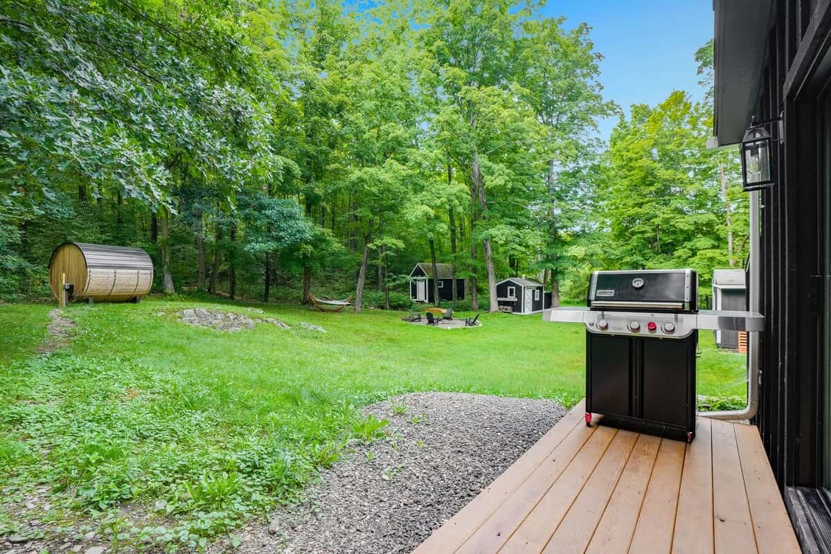 From the back deck: the gas grill, the lawn, and the sauna small against the tree line