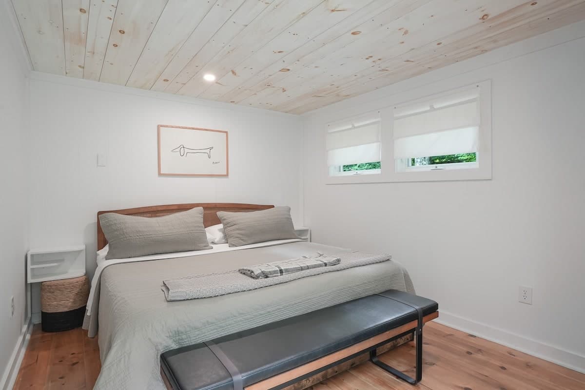 The bedroom: a king bed under a whitewashed pine ceiling, with a bench at the foot of the bed