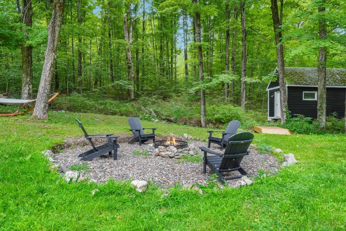 The firepit: a ring of fieldstone with four Adirondack chairs at the edge of the woods, a fire going