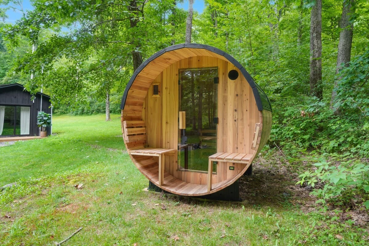 The cedar barrel sauna standing in the trees behind the cabin, its door open